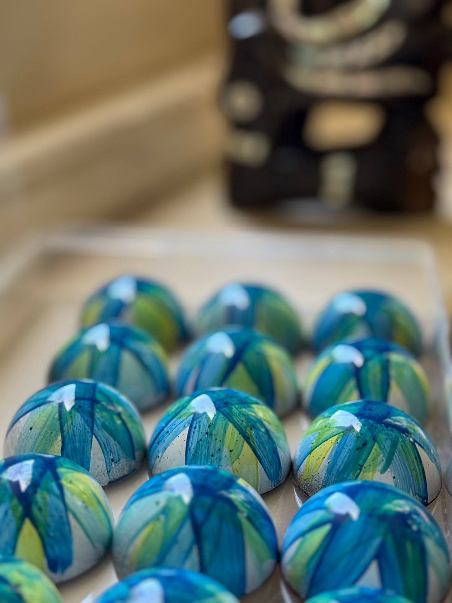 Blue and green chocolate bonbons on a clear tray with a blurred background