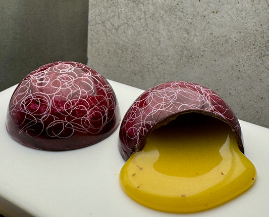 Two hand-painted passionfruit caramel bonbons, one cut open with the yellow caramel flowing out